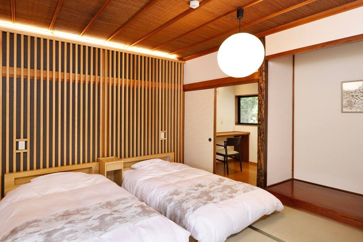 A room with two beds, a desk, and a large window.