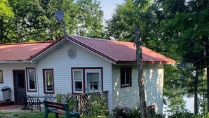 Une petite cabane blanche avec un toit rouge, un banc et un arbre devant.