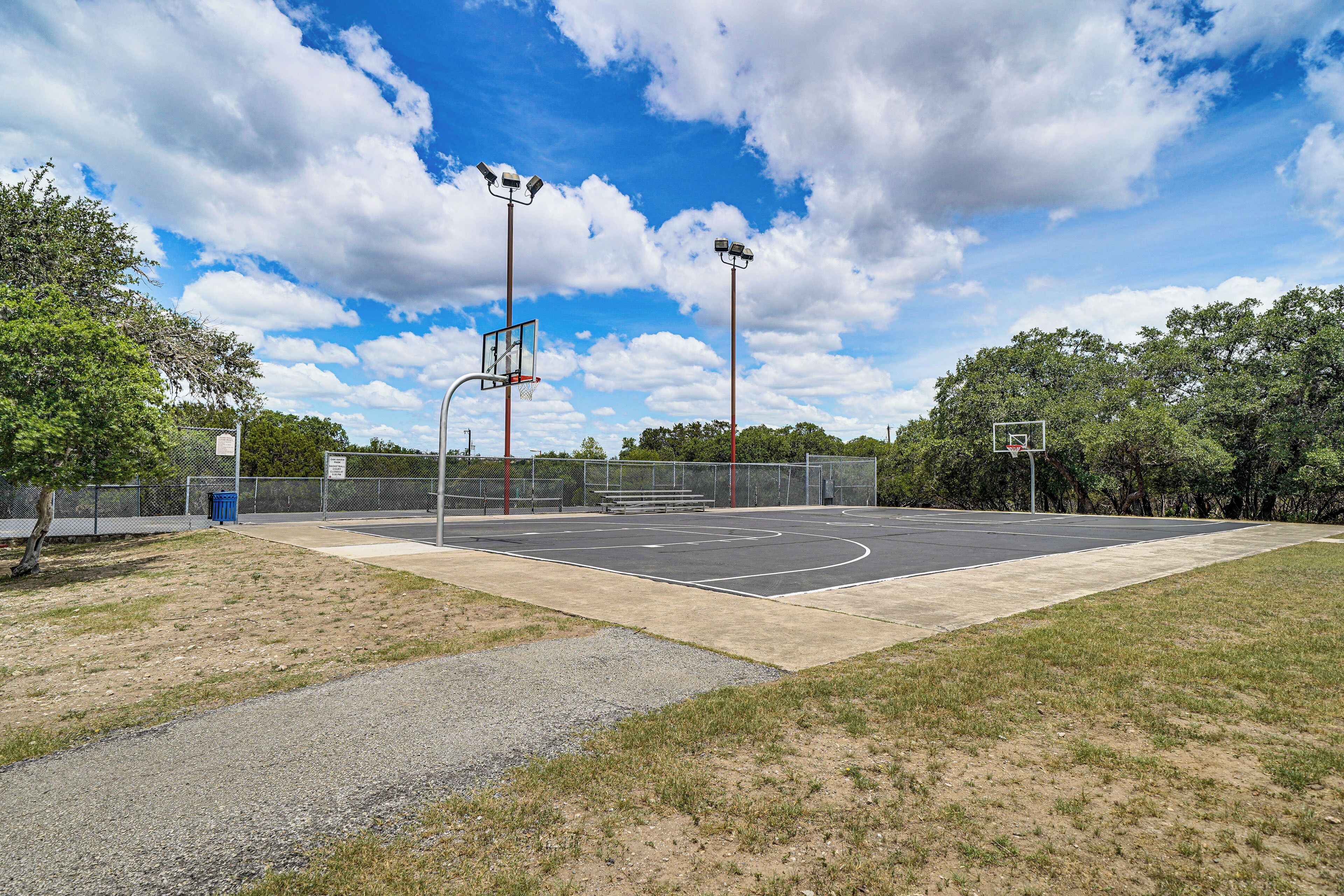An outdoor basketball court with a net, basketball hoops, and a fence.