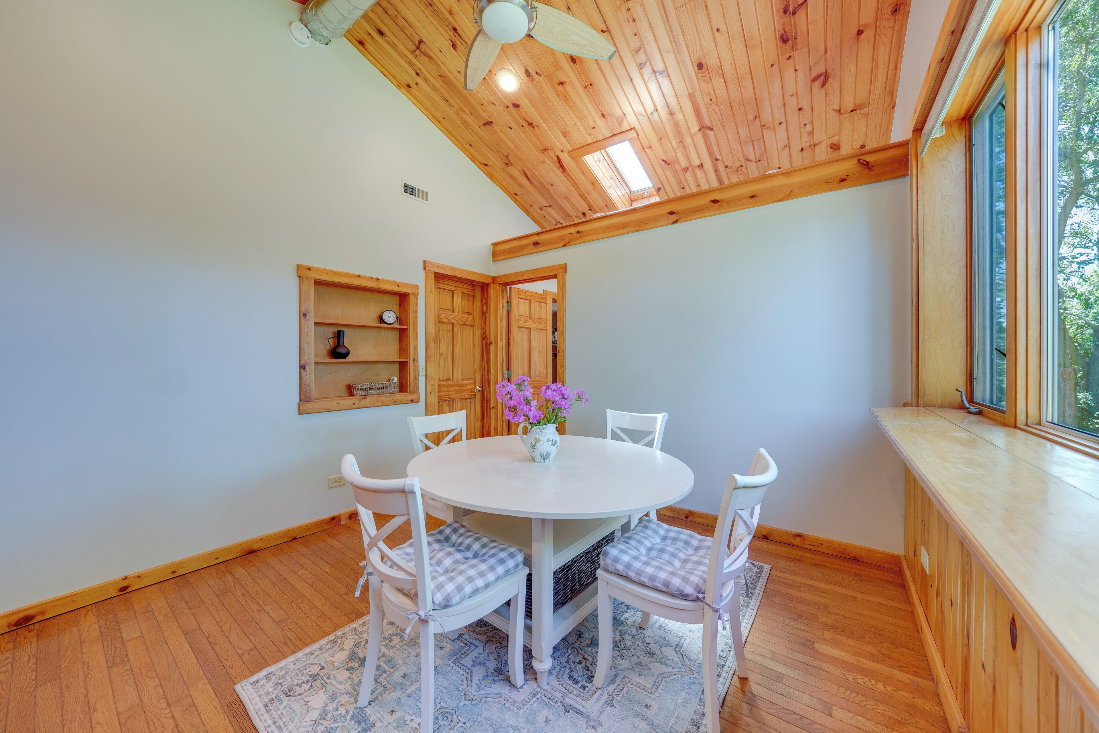 A dining area with a round table, white chairs, and a vase of purple flowers.