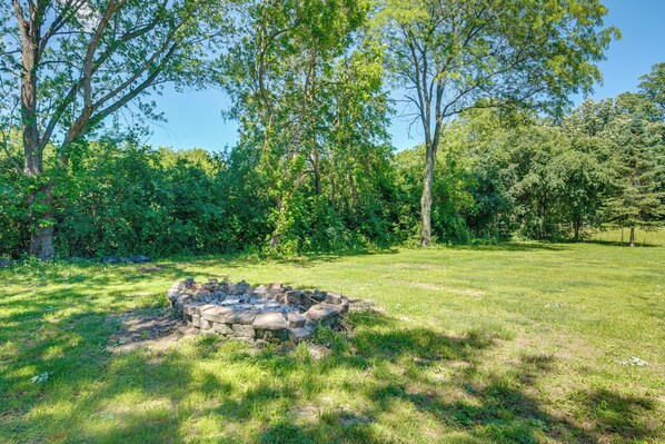 A stone fire pit surrounded by lush greenery and trees.