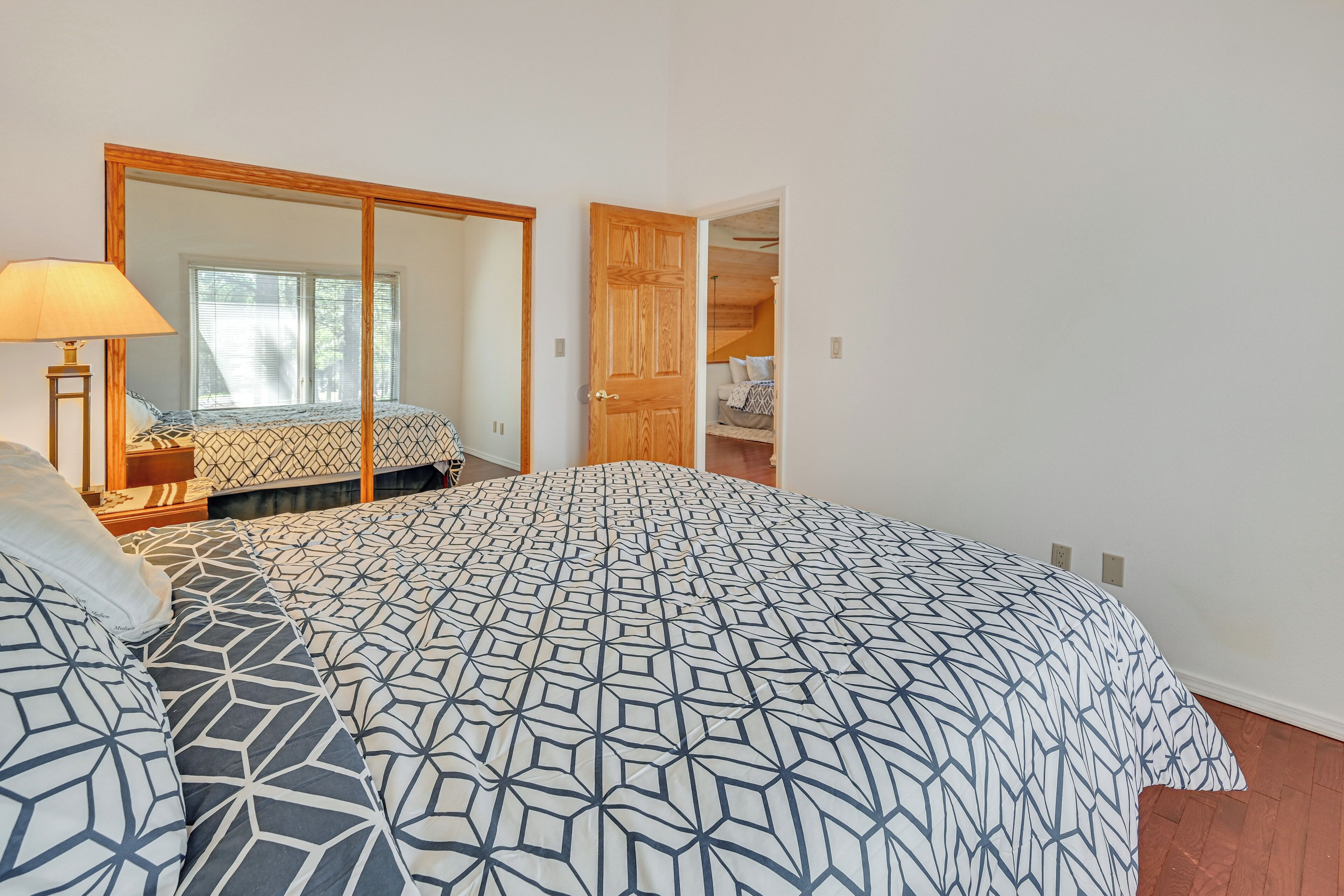 A bedroom with a large bed, a mirror, and a wooden door leading to a closet.