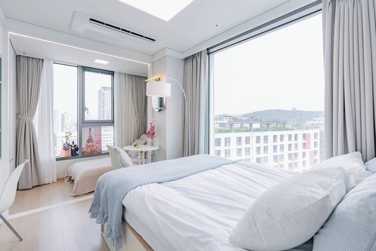 A modern hotel room with a large bed, a desk, and a view of the cityscape.