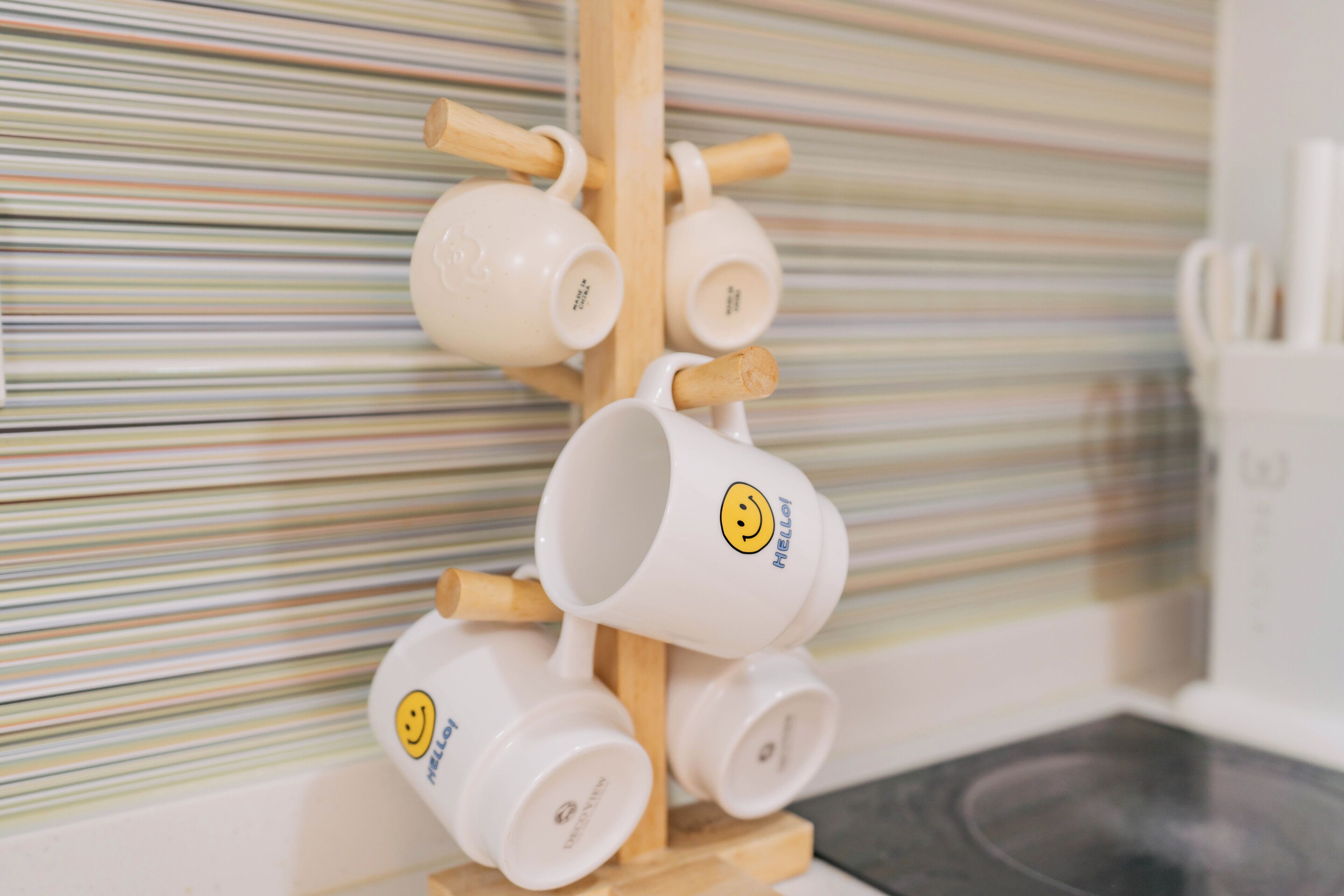 A set of white mugs with smiley faces on a wooden stand against a striped wall.