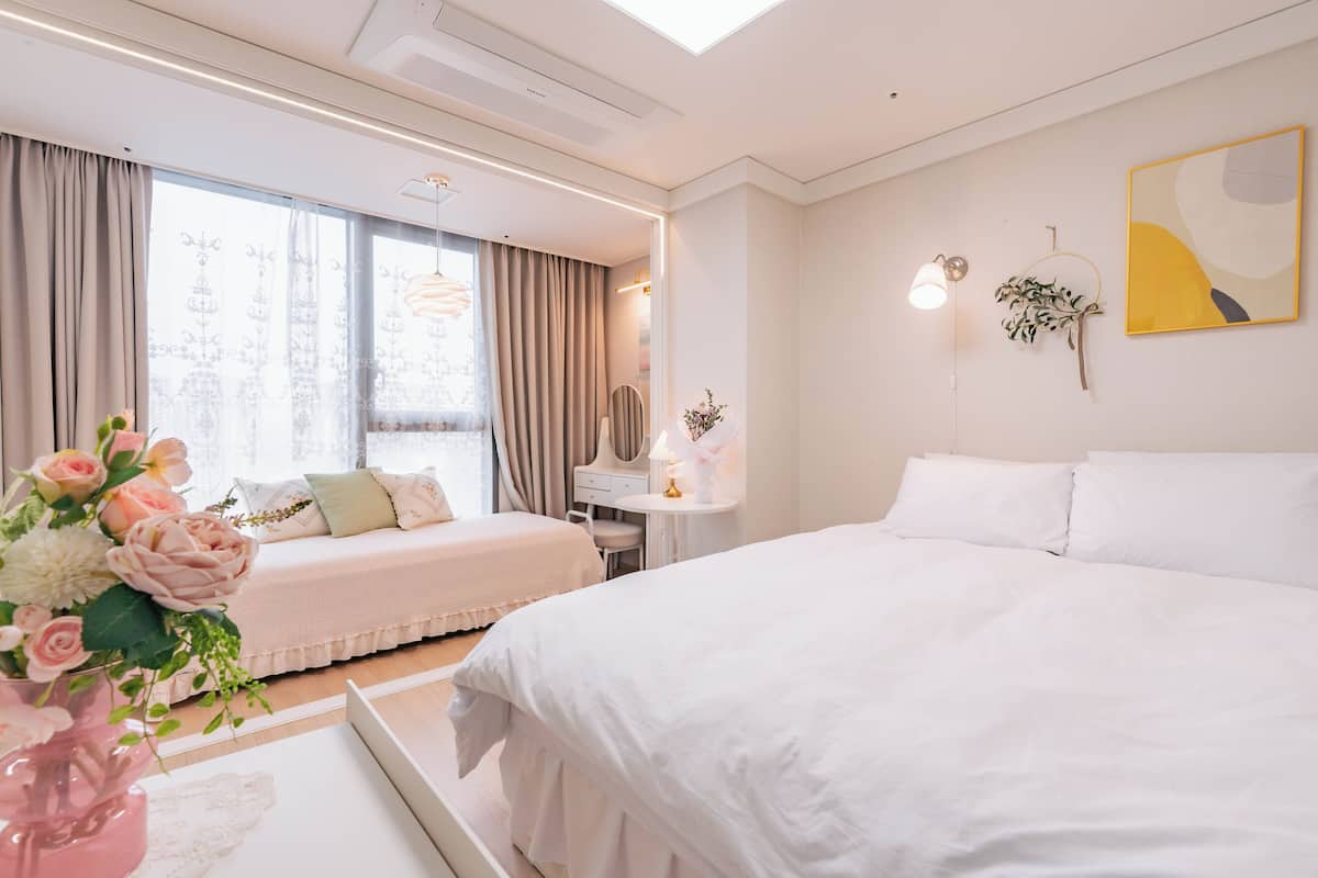 A modern hotel room with a large bed, a smaller bed, a desk, and a vanity.