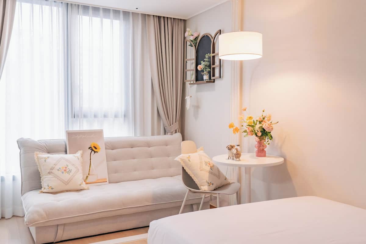 A hotel room with a sofa, a small table with a vase of flowers, and a lamp.