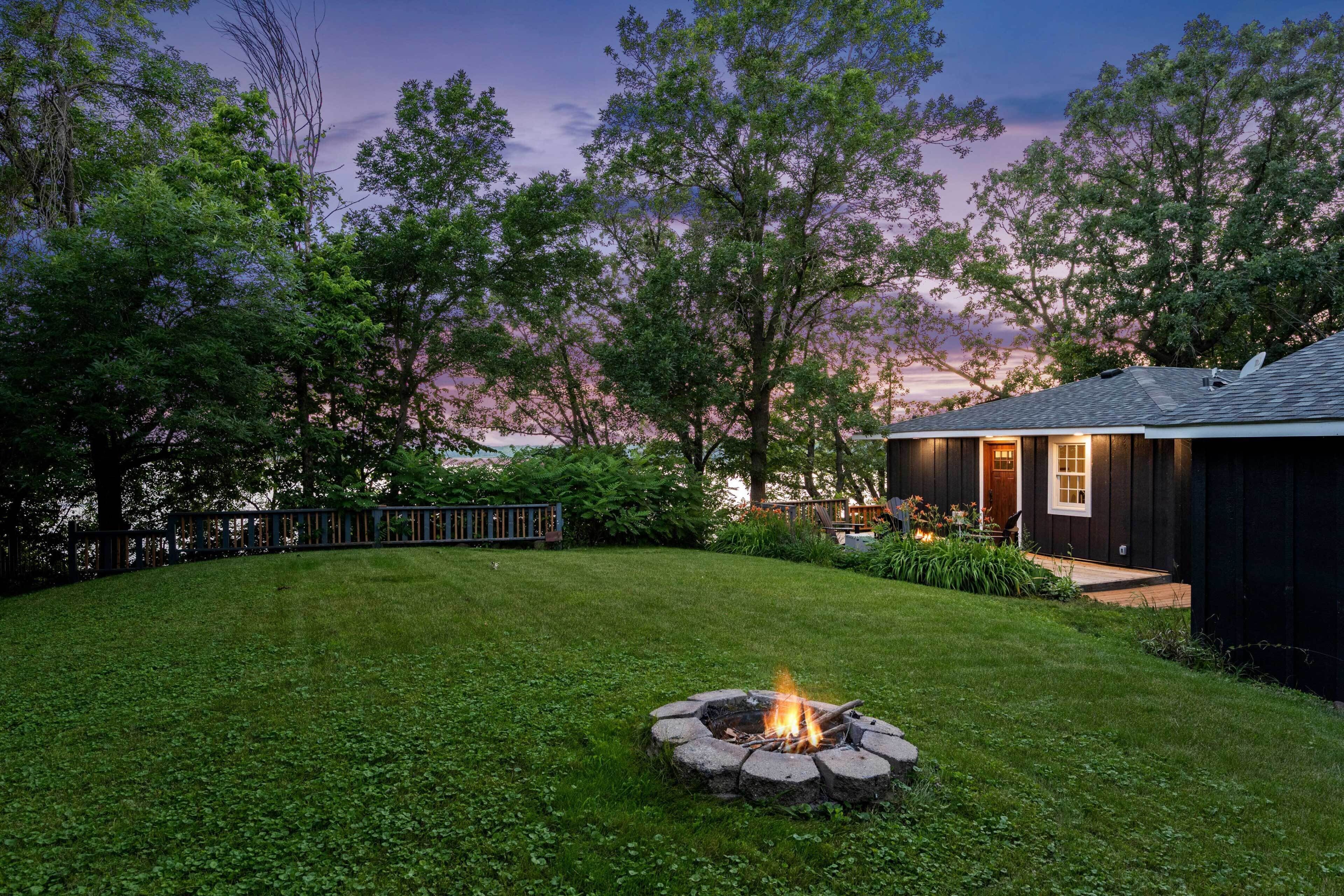A backyard with a fire pit, a wooden deck, and a house with a dark exterior.