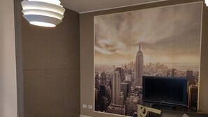 Ett vardagsrum med en stor väggmålning som föreställer en stadsbild, en platt-TV, en soffa och en modern hänglampa.