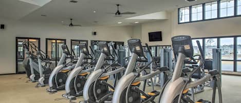 A gym with multiple stationary bikes, large windows, and ceiling fans.