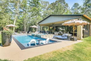 A pool area with lounge chairs and umbrellas, a covered seating area, and a building with large windows. - Lake Murray Paradise w/ Shared Pool & Hot Tub! (Prosperity)