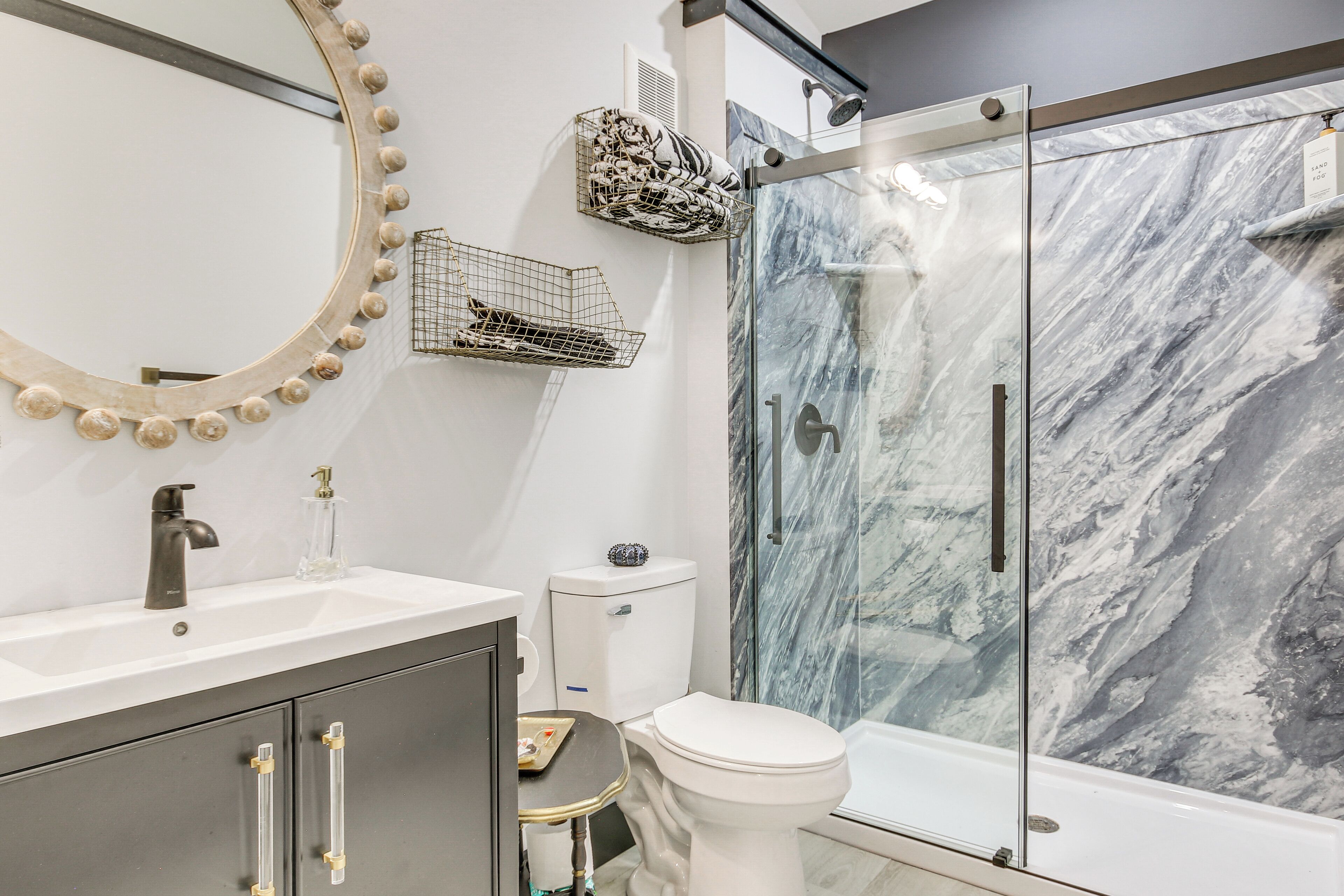 A modern bathroom with a marble shower, a white toilet, and a vanity with a mirror and sink.