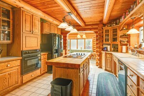A log cabin kitchen with wooden cabinets, a central island, and a large refrigerator. - Indoor Pool & Hot Tub! Spacious Sterling Cabin (Alger)