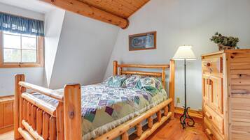 A wooden bed with a quilt, a wooden dresser, a lamp, and a framed picture on the wall.