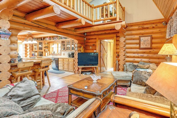 A log cabin interior with a dining area, a living room with a sofa and armchairs, a television, and a kitchen area. - Indoor Pool & Hot Tub! Spacious Sterling Cabin (Alger)