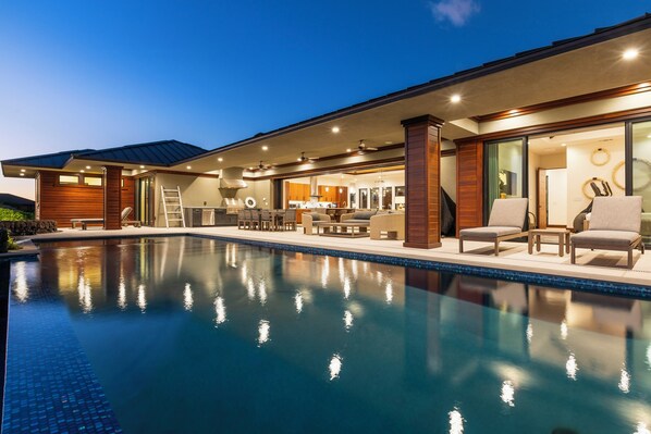 A modern house with a swimming pool, outdoor furniture, and a well-lit interior.
