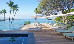 A poolside area with lounge chairs and umbrellas, overlooking a body of water with palm trees.