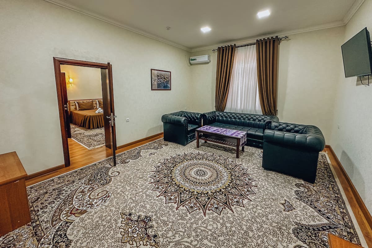 Una sala de estar con alfombra estampada, un sofá de color oscuro, una mesita de centro y una puerta que da a otra habitación.
