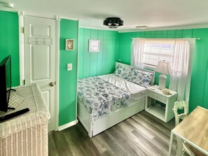 Una habitación con una cama, una mesita, una silla, una lámpara y un televisor.