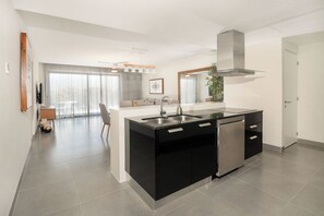 Modern kitchen with a central island, stainless steel sink, and dishwasher, adjacent to a seating area with a sofa and coffee table.