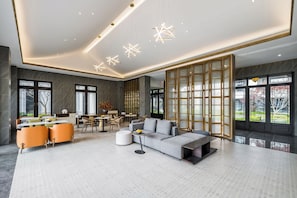 A spacious living area with a grey sofa, orange chairs, and a dining table. - Poltton Century Hotel (Changtai Taoli Chunfeng Branch) (Zhangzhou)
