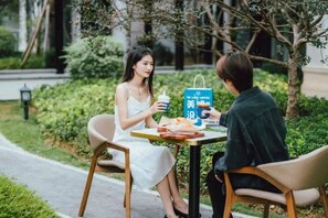 Two people sitting at an outdoor table with a menu and drinks, surrounded by greenery. - Poltton Century Hotel Changtai Taoli  (Zhangzhou)