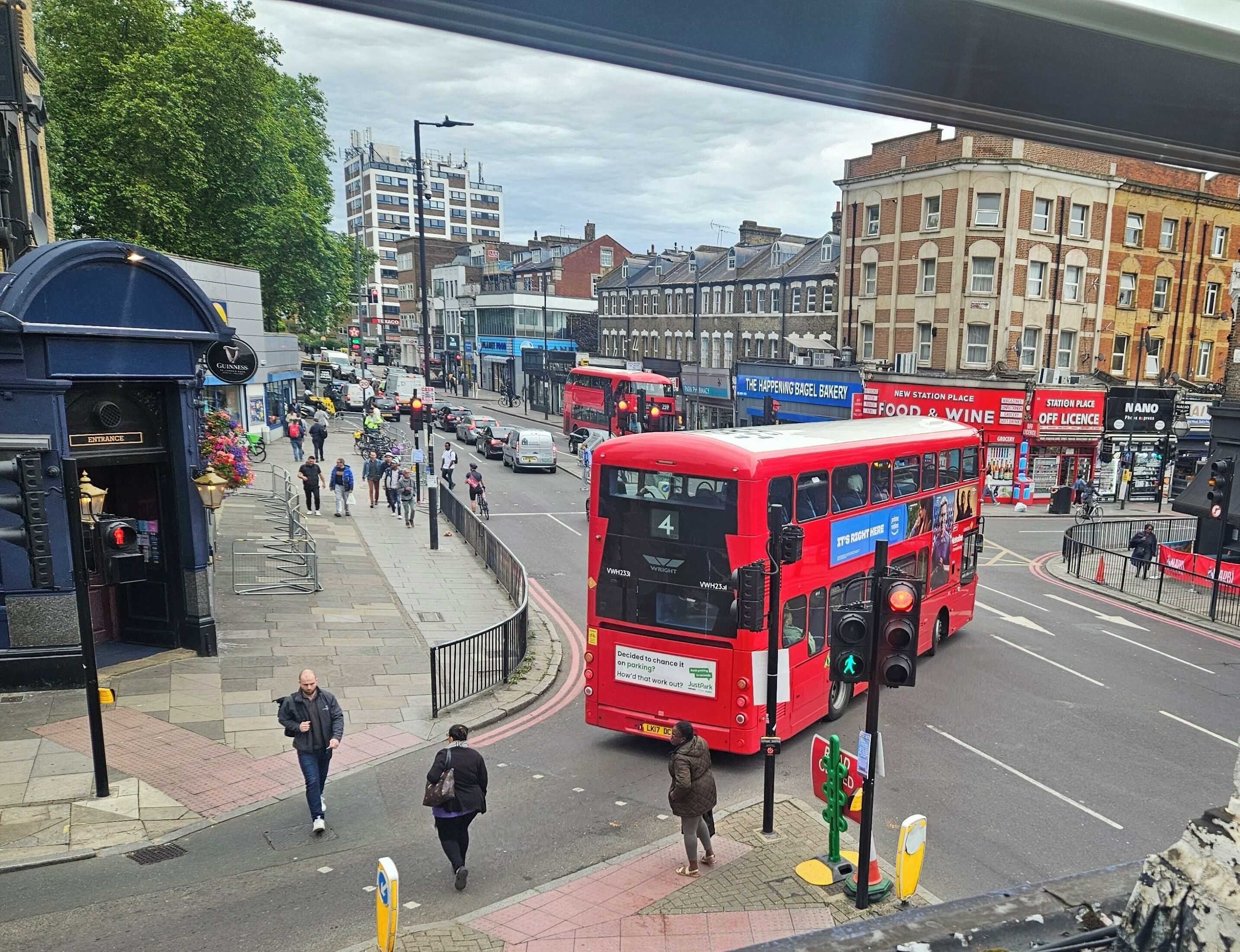 A busy urban street with a red double-decker bus, pedestrians, and various shops.