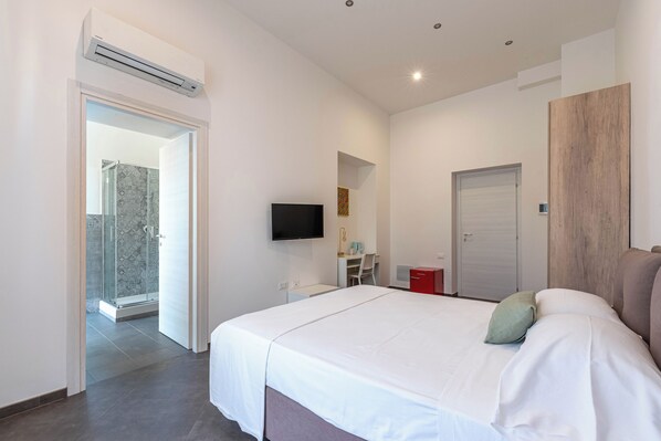 A modern hotel room with a large bed, a TV mounted on the wall, a shower area, and a wooden accent wall. - Apartments La Cala by Wonderful Italy (Palermo)