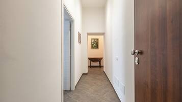A narrow hallway with a wooden door on the right and a table with a chair in the distance.