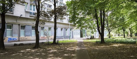 Un chemin bordé d’arbres mène à un bâtiment doté de nombreuses fenêtres et de balcons.