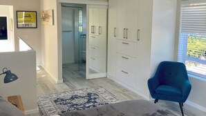 A modern bedroom with a bed, a blue armchair, and a wardrobe. - LUXURIOUS TWO-STORY SELF-CATERING RETREAT IN THE HEART OF THE CAPE WINELANDS 
 (Somerset West)