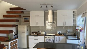 A modern kitchen with white cabinets, a stainless steel range hood, and a central island with bar stools. - LUXURIOUS TWO-STORY SELF-CATERING RETREAT IN THE HEART OF THE CAPE WINELANDS 
 (Somerset West)