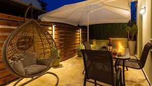 Un patio exterior con una silla colgante, una mesa con velas y un paraguas blanco.