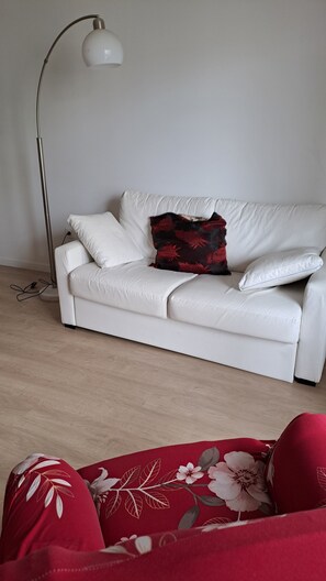 Relax on the white leather sofa in this inviting living space, featuring a floor lamp and a cozy throw blanket.