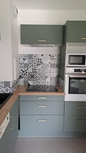 Compact kitchen with microwave, oven, and sink, featuring a unique backsplash with geometric and floral tile patterns.