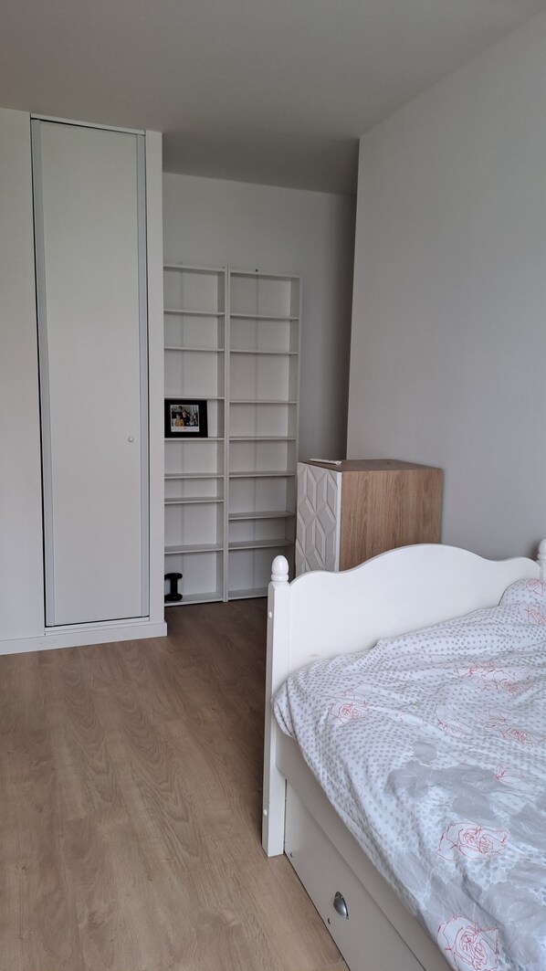 Cozy retreat with a neatly arranged bed, white wardrobe, and convenient bedside table with lamp.