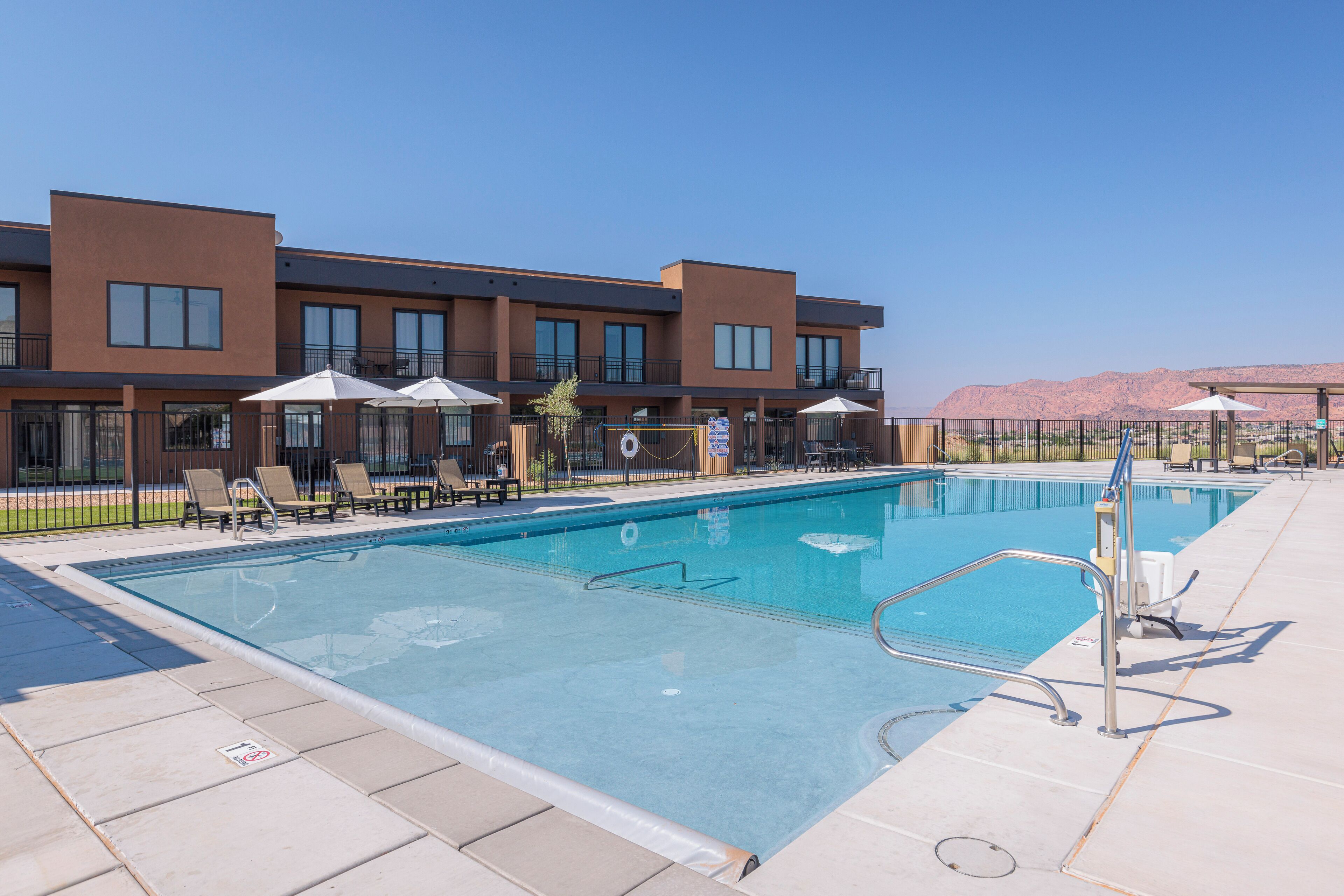 A swimming pool with lounge chairs and umbrellas, surrounded by a building with multiple windows and balconies.