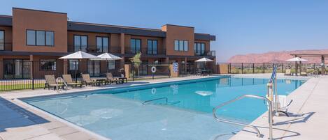 A swimming pool with lounge chairs and umbrellas, surrounded by a building with multiple windows and balconies.
