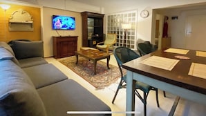 Una sala de estar con sofá, mesa de centro y televisor. Se observa una mesa de comedor con sillas y una alfombra.