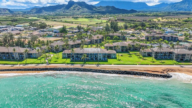 A coastal resort with multiple hotel buildings, a beach, and a mountainous backdrop. - Pono Kai Resort J201, 2nd Floor, Walk to Beach (Kapaa)