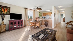 A spacious living area with a dining table, a television, and a kitchen in the background. - Pono Kai Resort J201, 2nd Floor, Walk to Beach (Kapaa)