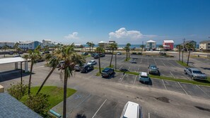Un estacionamiento con varios coches, palmeras y edificios al fondo.