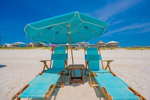 A beach chair and umbrella setup with a clear view of beachfront properties in the background.