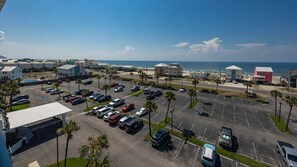 A parking lot with multiple cars, a beach in the background, and several buildings including a red structure.