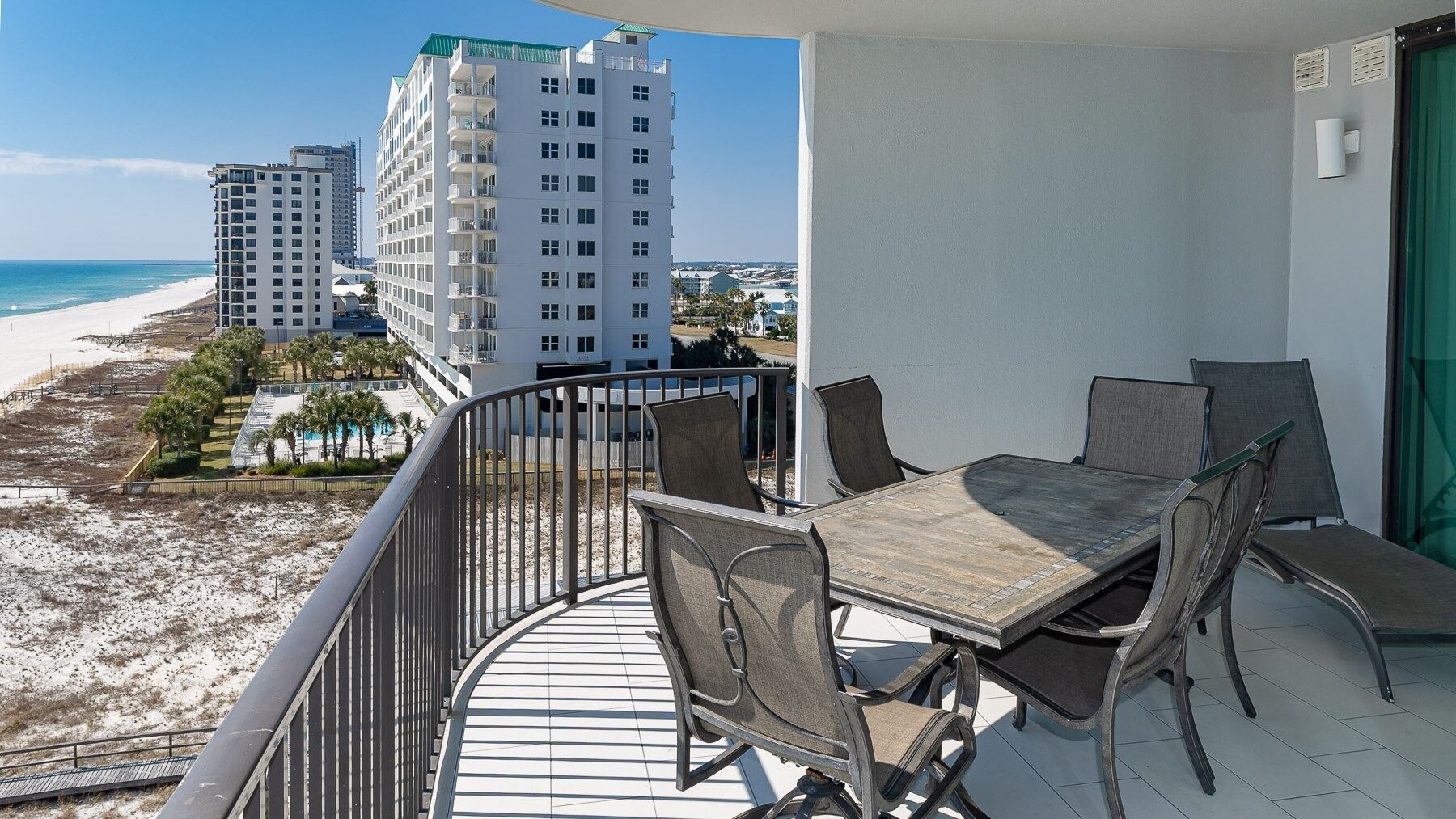 A balcony with a table and chairs overlooking a beach and hotel buildings.