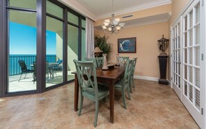 A dining area with a table set for six, surrounded by chairs, a chandelier, and a painting on the wall. - Phoenix West 1202 3 Bedroom Condo (Orange Beach)
