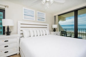 A bedroom with a large bed, two bedside tables, a ceiling fan, and a balcony with a view of the beach. - Island Winds West 2723-4 4 Bedroom Condo (Gulf Shores)