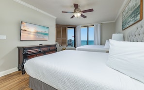 A hotel room with a bed, a ceiling fan, a TV, a painting, and a view of the ocean. - Phoenix X 617 3 Bedroom Condo (Orange Beach)