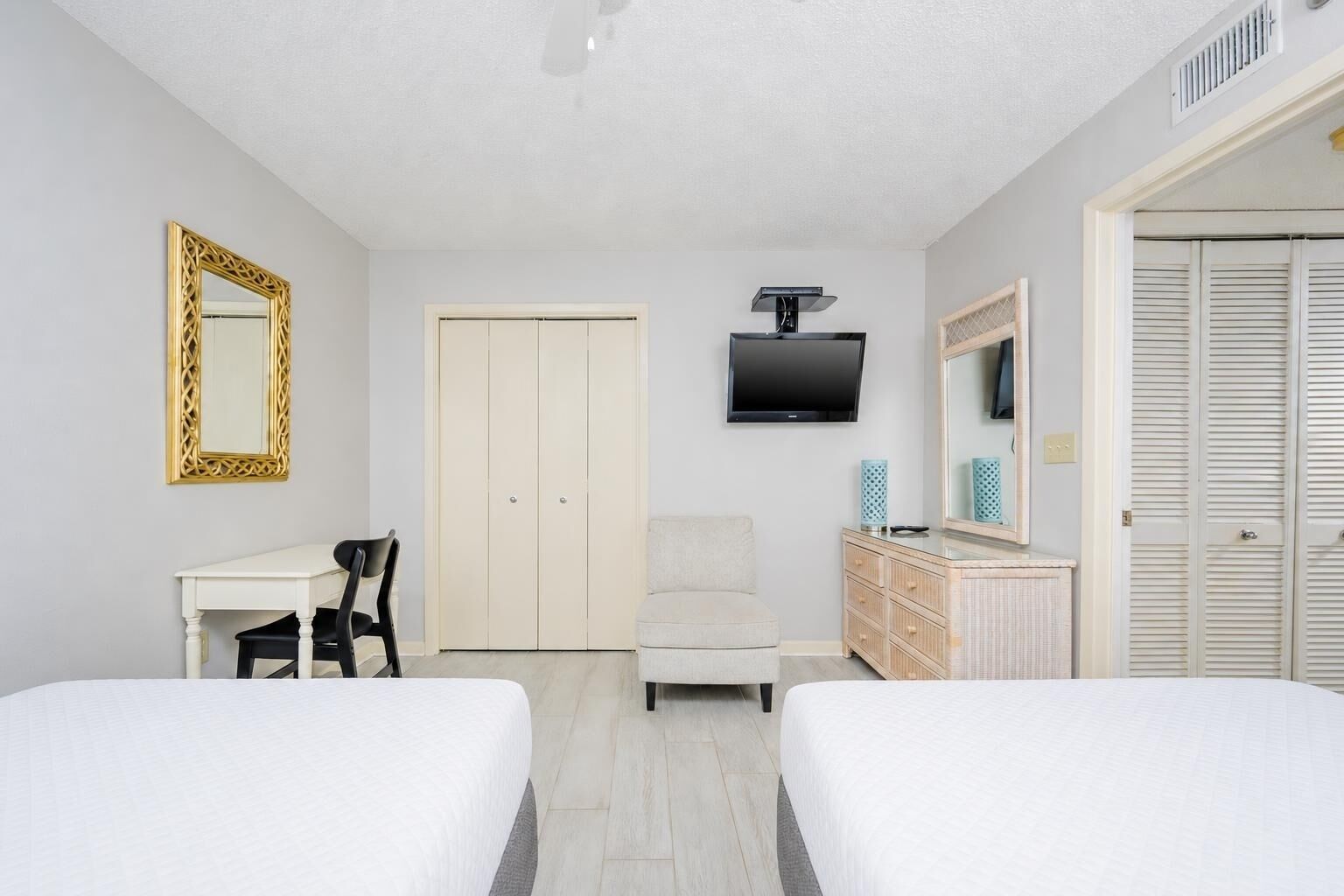 A hotel room with two beds, a desk, a chair, a TV, a wardrobe, and a mirror.