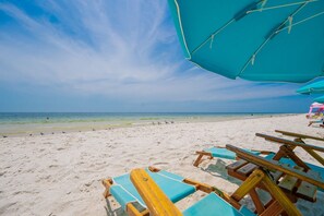Ein Strand mit blauem Himmel, sandigem Ufer und Holzliegen.