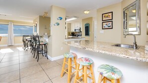 A kitchen with a large island, bar stools, and a view to the outside. - Gulf Shores Surf & Racquet 801a 3 Bedroom Condo (Gulf Shores)